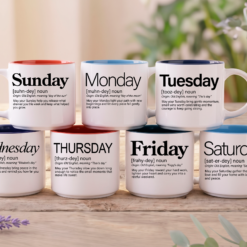 Seven Day of the Week Blessing mugs, Sunday through Saturday, 14-ounce white stackable mugs with Word Story Style™ blessings in different fonts and red, blue and black interiors, stacked on a wooden table with lavender.